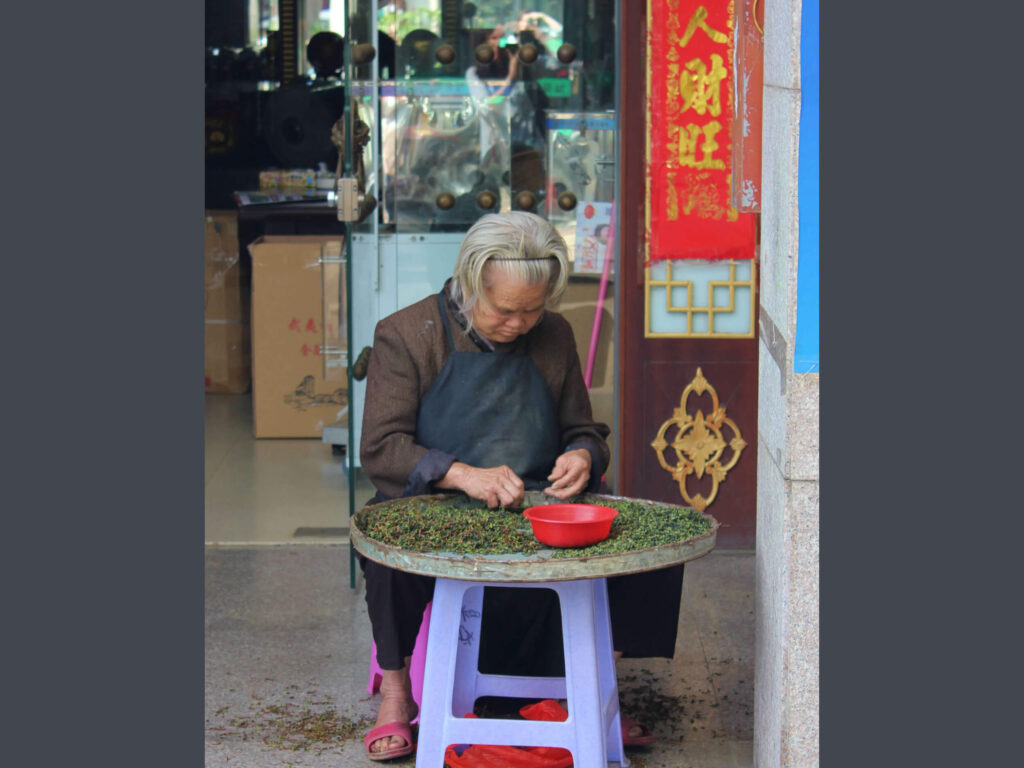 old woman sitting outside tea ship, sorting tea