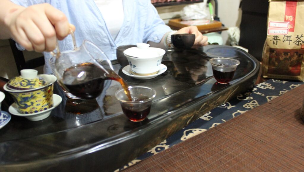 dark tea liquor being poured from glass jug into tea cup, gongfu