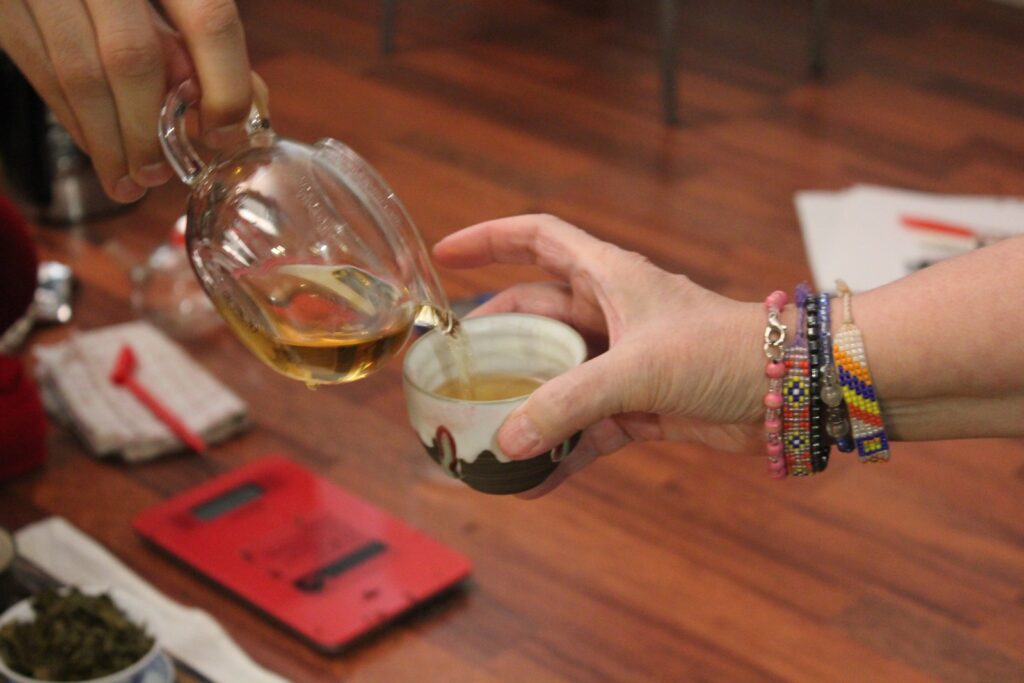 Autumn Mang Fei tea being poured from glass jug into tea cup held by a hand