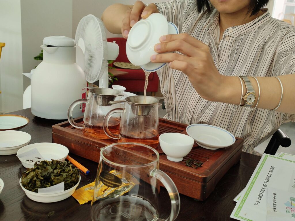 Pouring Oolong TeeMaa2 pouring tea from gaiwan to glass jug, on wooden tea tray