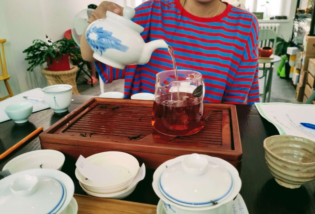 PouringTea_Red pouring tea from teapot into glass jug, on a wooden tea tray
