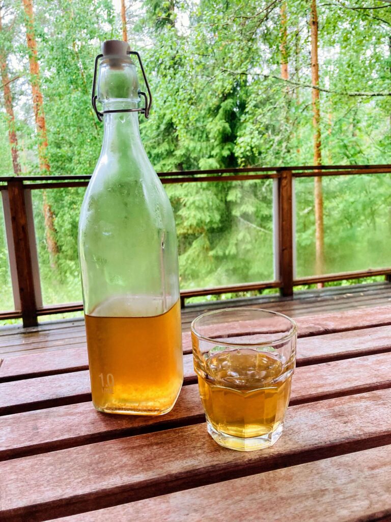 IMG_7556 bottle and glass of kombucha, wooden balcony, forest background