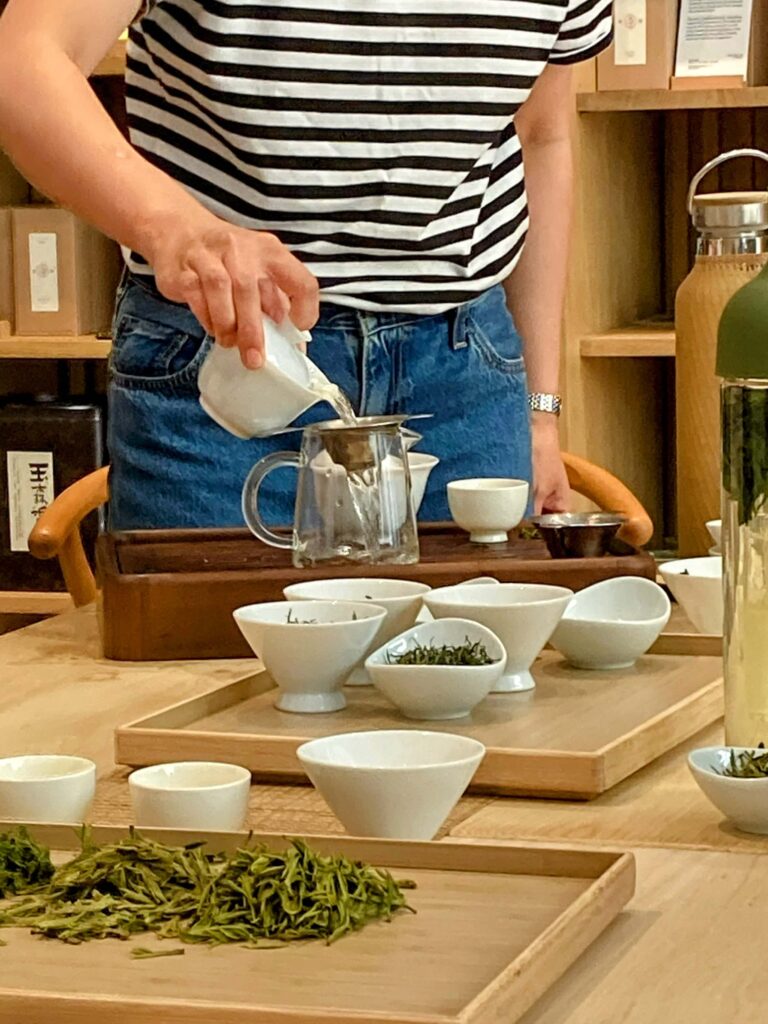 someone making gongfu tea, with several white cups and tea leaves in the foreground